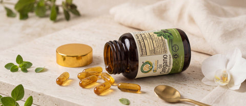 Botella de cápsulas de aceite de orégano OreganicUSA recostada con cápsulas visibles alrededor en una escena botánica lujosa y realista.